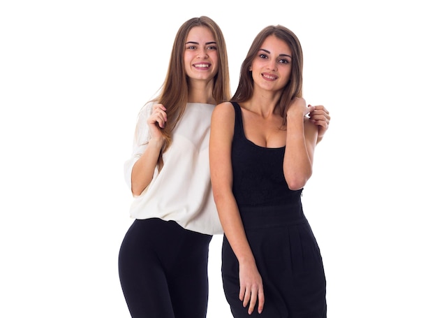 Duas jovens mulheres bonitas em camisas pretas e brancas abraçando em fundo branco no estúdio