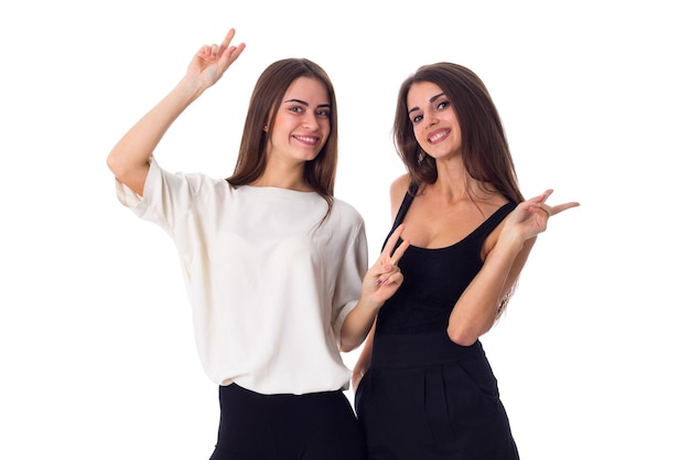 Duas jovens mulheres bonitas em camisas pretas e brancas mostrando paz em fundo branco no estúdio