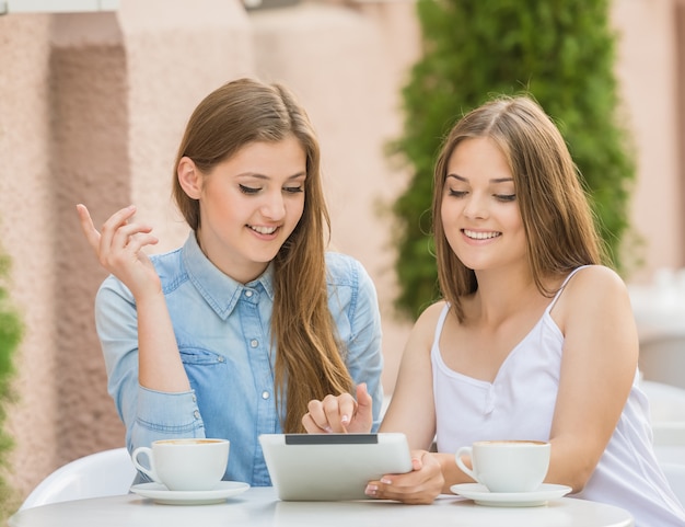 Duas jovens mulheres bonitas que sentam-se no café do verão.