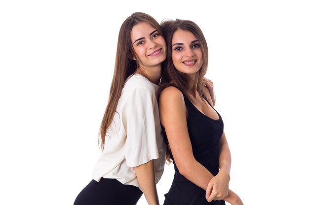 Duas jovens mulheres felizes em camisas brancas e pretas abraçando em fundo branco no estúdio