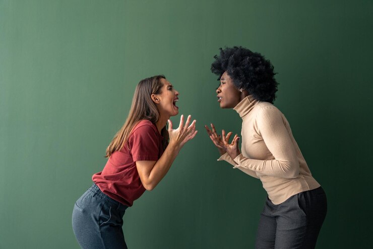 Foto duas jovens mulheres interraciais furiosas gritando uma com a outra contra um fundo verde em um estúdio