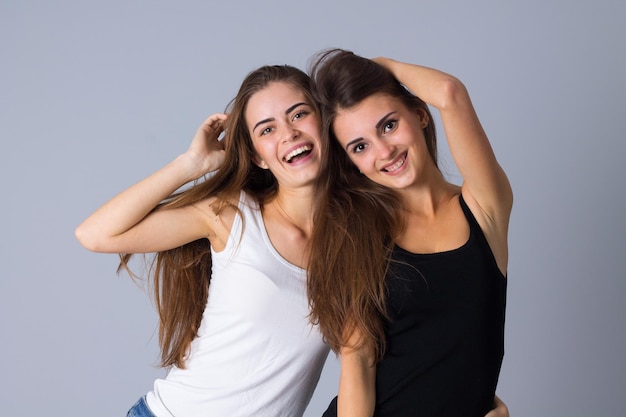 Duas jovens mulheres sorridentes em camisas pretas e brancas abraçando em fundo cinza no estúdio