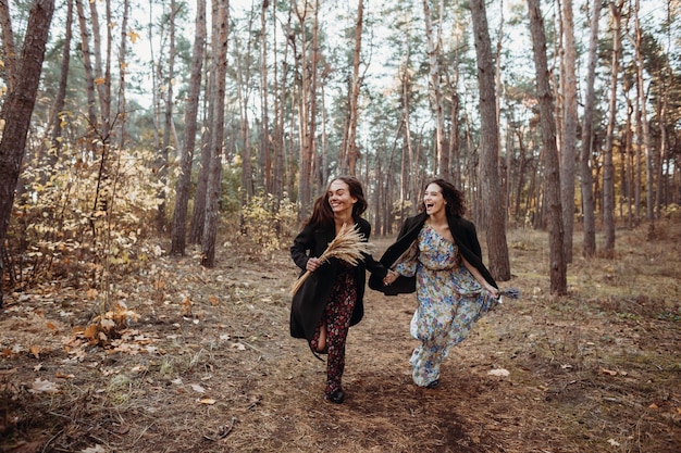 Duas jovens se divertindo correndo pela floresta de outono de mãos dadas