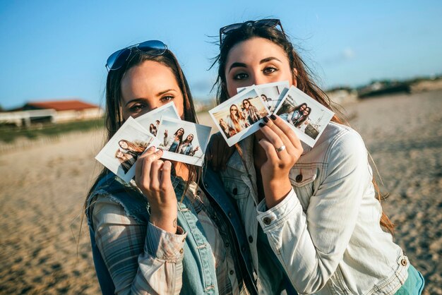 Duas jovens segurando fotos instantâneas na frente de seus rostos