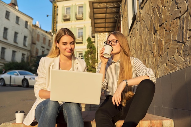 Duas jovens sorridentes olhando para o monitor do laptop sentado ao ar livre