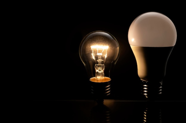 Duas lâmpadas em um fundo preto uma lâmpada incandescente está brilhando e um conceito de lâmpada LED de tecnologia elétrica