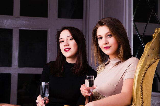 Duas linda garota elegante sexy em vestidos de noite bebem champanhe em um quarto de luxo