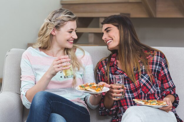 Duas linda mulher sentada no sofá e comer pizza