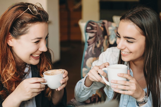 Duas linda mulher tomando café e rindo enquanto conta histórias enquanto está sentado em um café.