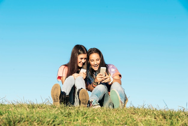 Duas lindas adolescentes usando o celular no parque