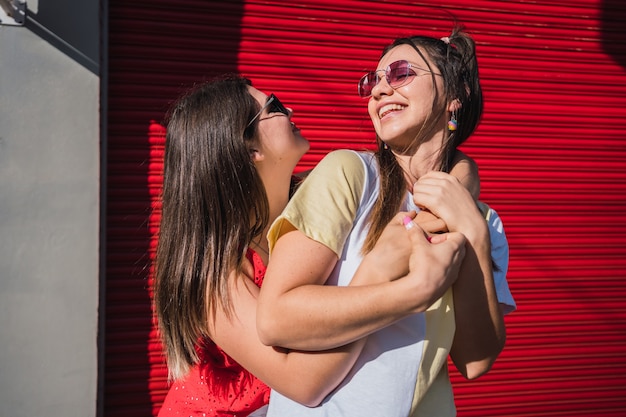 Duas lindas amigas estão torcendo e rindo com óculos escuros.