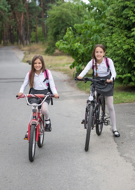 Duas lindas colegiais indo para a escola em bicicletas