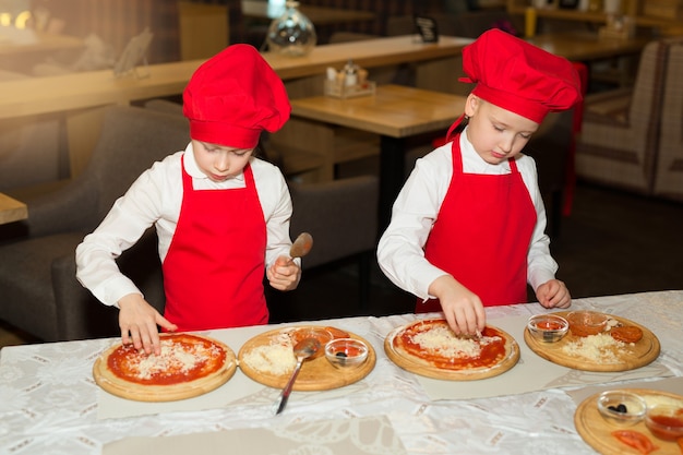 duas lindas cozinheiras de camisa branca e avental vermelho no restaurante fazendo pizza