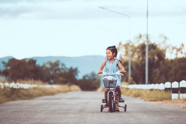 Duas lindas crianças de meninas asiáticas se divertindo para andar de bicicleta juntos no parque