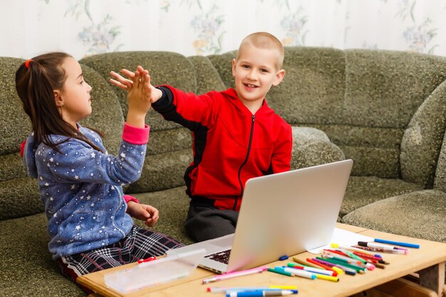 Duas lindas e felizes crianças sorridentes, um menino e uma menina, usam laptop para ensino à distância ou entretenimento.