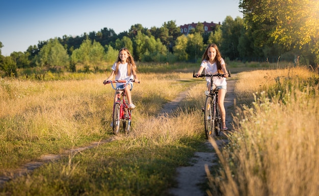 Duas lindas garotas andando de bicicleta em um prado em um dia de sol