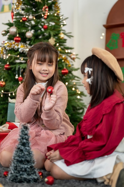 Duas lindas garotas asiáticas estão brincando juntas na sala de estar em uma noite de Natal