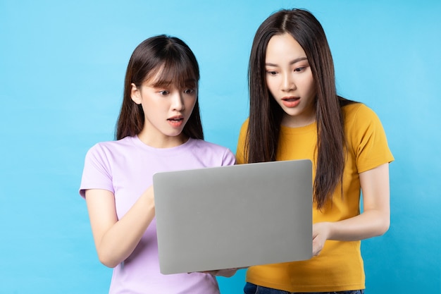 Duas lindas garotas asiáticas usando laptop na parede azul