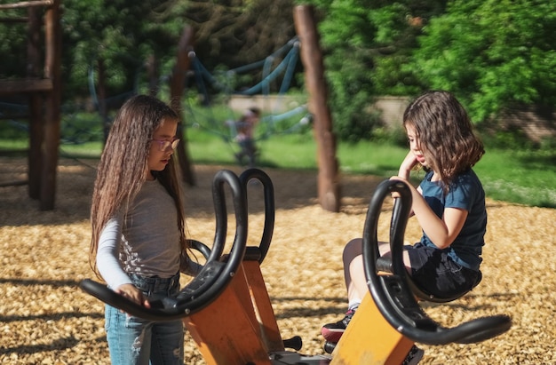 Duas lindas garotas caucasianas se levantam e se comunicam em um balanço giratório no parque