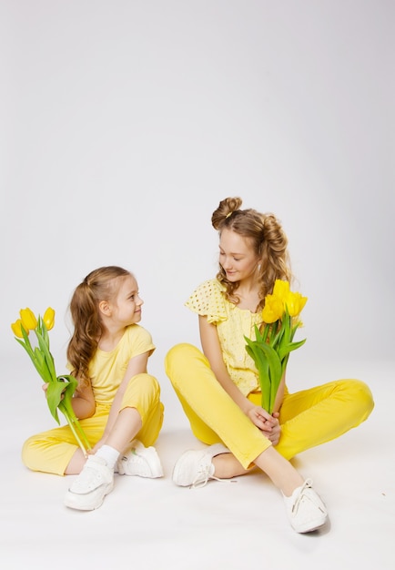 Duas lindas garotas com cabelo loiro com tulipas amarelas em roupas amarelas