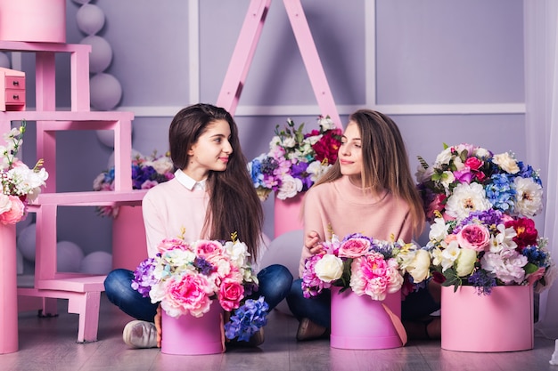 Duas lindas garotas em jeans e suéter rosa em estúdio com decoração de flores em cestas.