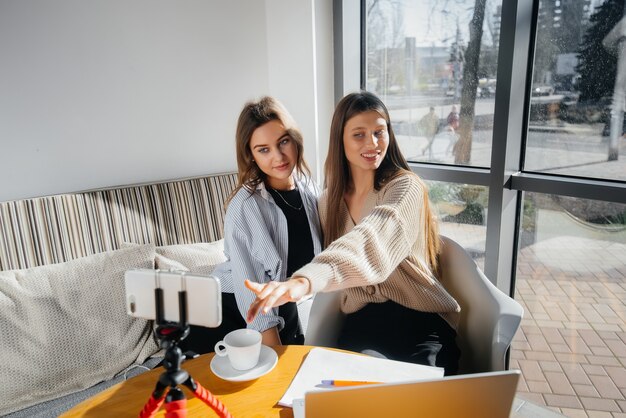 Duas lindas garotas estão sentadas em um café, gravando blogs de vídeo e se comunicando nas redes sociais.