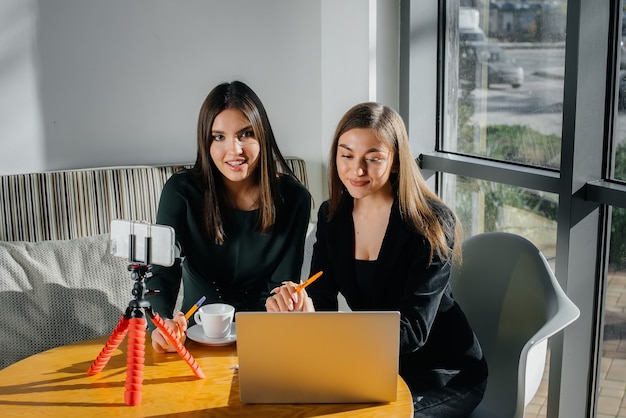 Duas lindas garotas estão sentadas em um café, gravando blogs de vídeo e se comunicando nas redes sociais.