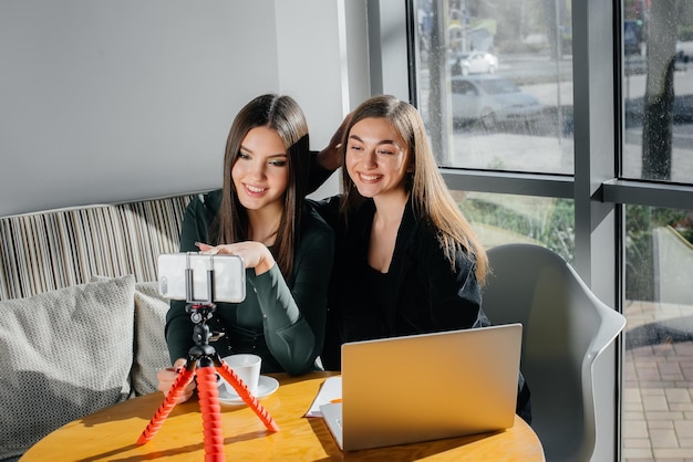 Duas lindas garotas estão sentadas em um café, gravando blogs de vídeo e se comunicando nas redes sociais.