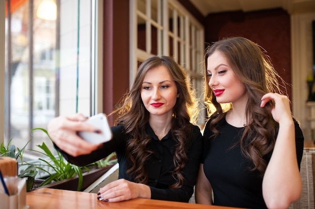 Duas lindas garotas fazendo selfi e tomando café