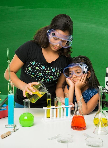 Duas lindas garotas indianas ou asiáticas experimentando ou estudando ciências em laboratório, sobre fundo de quadro verde com rabiscos educacionais