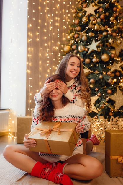 Duas lindas garotas na véspera de ano novo. Melhores amigas da jovem comemorando o Natal em casa. Prazer amizade nunca termina o conceito. Lindas decorações douradas de Natal em uma alta árvore de Natal