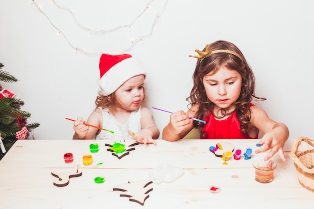 Duas lindas garotas pintando estatuetas de natal em madeira