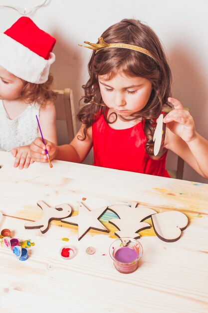 Duas lindas garotas pintando estatuetas de Natal em madeira