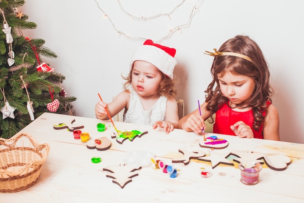 Duas lindas garotas pintando estatuetas de Natal em madeira