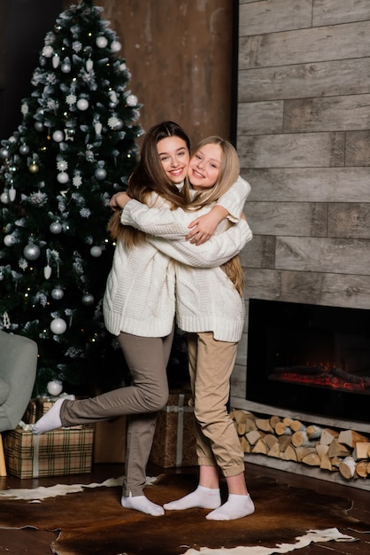 Duas lindas garotas posando com beijos de expressão facial com árvore de Natal. Mulher europeia de cabelos compridos ao lado de uma árvore e presentes