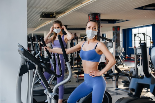 Duas lindas garotas se exercitam na academia usando máscaras durante a pandemia