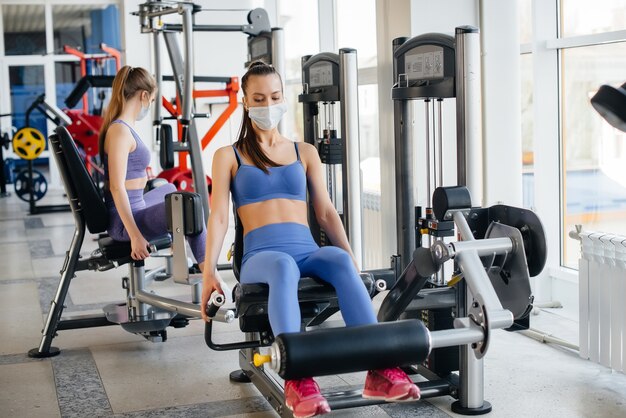 Duas lindas garotas se exercitam na academia usando máscaras durante a pandemia