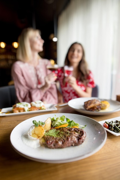 Foto duas lindas garotas sorridentes bebem coquetéis e comem comida deliciosa em um café