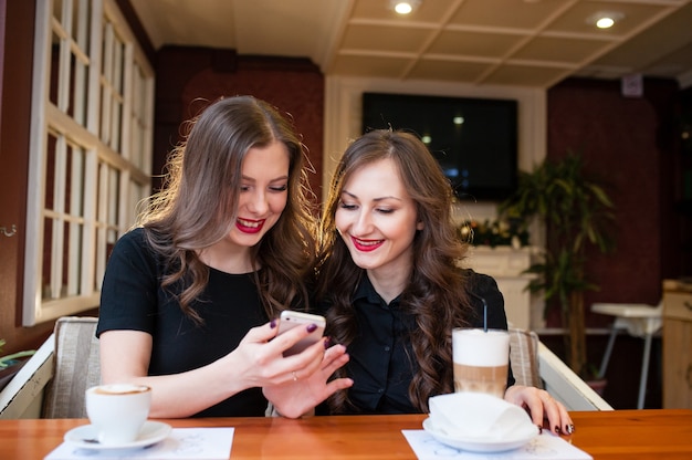 Duas lindas garotas tomam café e olham no telefone