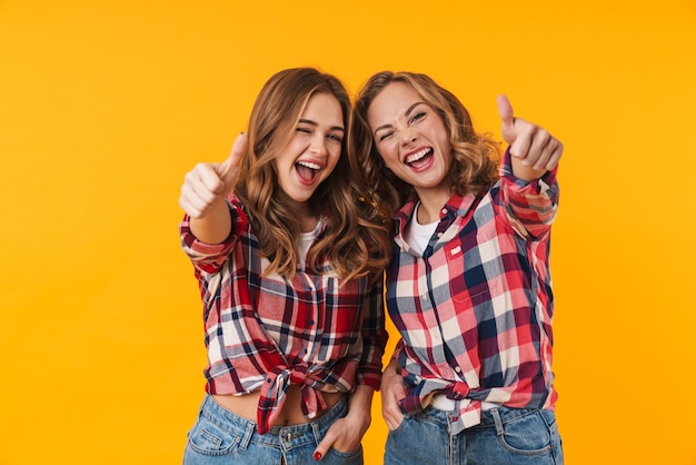 Duas lindas garotas vestindo camisa xadrez sorrindo e gesticulando com os polegares para cima isoladas