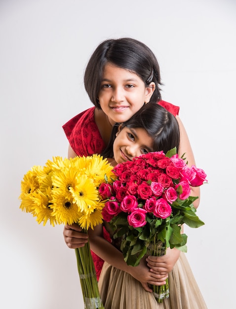 Duas lindas garotinhas indianas segurando um ramo ou buquê de rosas vermelhas frescas ou flores de gulab. isolado sobre fundo branco