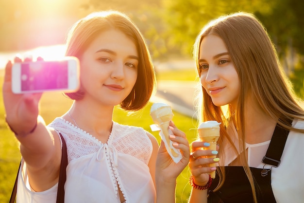 Duas lindas melhores amigas colegiais (estudante) fazendo selfie no telefone no parque