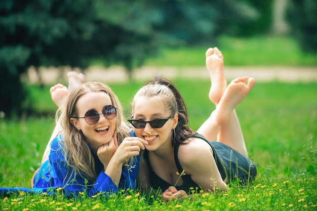 duas lindas meninas deitam na grama verde no parque e riem