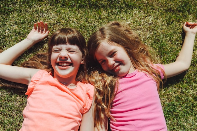 Duas lindas meninas deitam-se na grama verde na vista superior do parque de verão