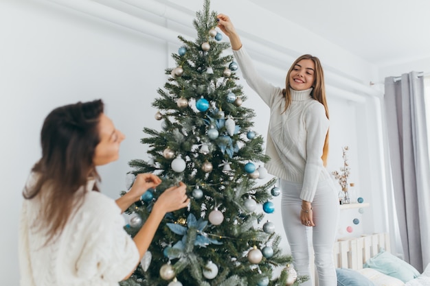 Duas lindas meninas estão decorando uma árvore de natal.