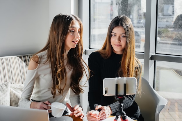 Duas lindas meninas estão sentadas em um café, gravando blogs de vídeo e se comunicando nas redes sociais.