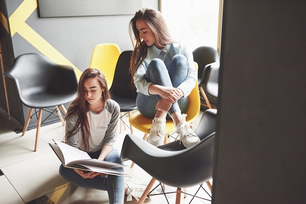 Duas lindas meninas gêmeas passam um tempo lendo um livro na biblioteca pela manhã. irmãs relaxando em um café e se divertindo juntos