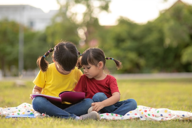 Duas lindas meninas lendo livros no jardim, sentado na grama. O conceito de educação e amizade.