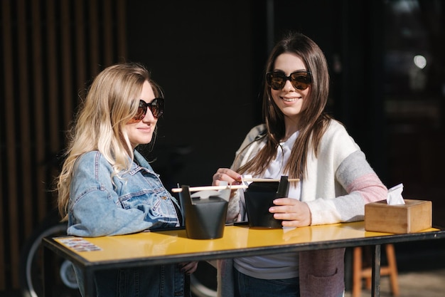 Duas lindas meninas loiras e morenas pedem comida chinesa para viagem jovem ao ar livre falando