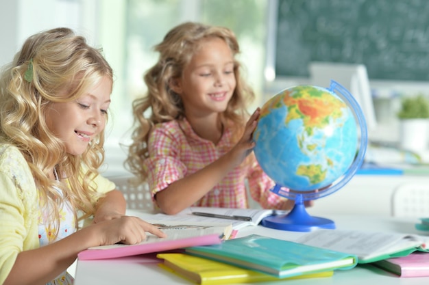 Duas lindas meninas na aula lendo livro e olhando para o globo
